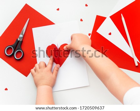 Kid makes Mother's Day or Valentine's Day greeting card. DIY holiday card with red paper volumetric heart, symbol of love. Handicraft made by child with scissors, glue and colored paper. Step 11 of 12