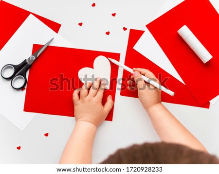 Kid makes Mother's Day or Valentine's Day greeting card. DIY holiday card with red paper volumetric heart, symbol of love. Handicraft made by child with scissors, glue and colored paper.Step 1 of 12.