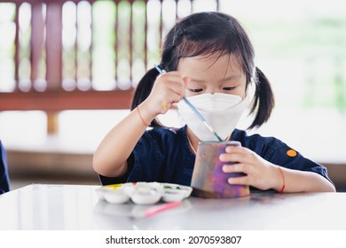 Kid making craft with paintbrush. Little girl wearing surgical white face mask to prevent spread virus and dust pollution PM2.5. - Powered by Shutterstock