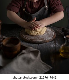 Kid Making Dough On Wooden Table With Ingredients Flour, Oil, Salt, Dark Background. Copy Space. Home Bakery Concept, Kitchen Cooking Story.