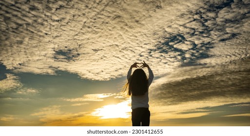 Kid making heart hands against the blue sky,child hands forming a heart shape with sunset silhouette