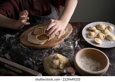 Kid Making Pelmeni (meet Dumplings) Of Dough On Wooden Table With Ingredients Flour, Oil, Salt, Dark Background. Copy Space. Home Bakery Concept, Kitchen Cooking Story.