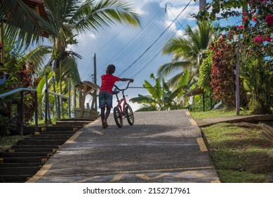 A Kid With No Shoes Dragging A Bike Uphill