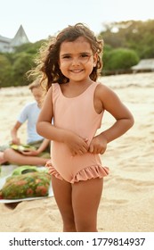 Kid On Beach Portrait. Tanned Little Girl In Swimsuit Standing On Sandy Coast And Looking At Camera. Summer Vacation With Children At Tropical Resort As Lifestyle.