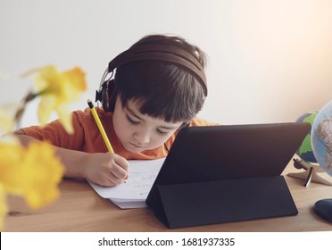 Kid online,Child using tablet for homework,Asian boy wearing headphones ,School kid reading and writing doing homework,Education with Technology for Home schooling concept 