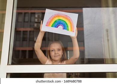 Kid painting rainbow during Covid-19 quarantine at home. Girl near window. Stay at home Social media campaign for coronavirus prevention, let's all be well, hope during coronavirus pandemic concept - Shutterstock ID 1689680788
