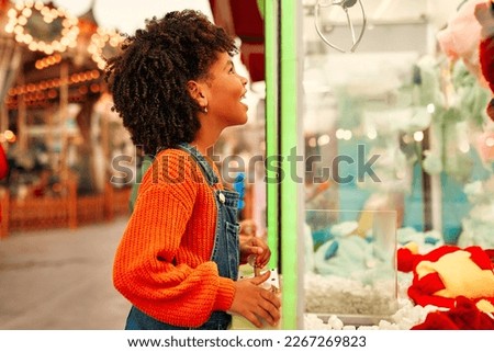 Kid play in the arcade center of the machine to get the claws of soft toys for coins. An African-American girl at amusement park.