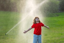 Kid Play In Garden Near Irrigation Watering Sprinkler System. Watering Grass With Automatic Sprinkler. Lawn And Gardening Concept. Child Backyard Gardening. Child Watering Plants, Watering Sprinkler.