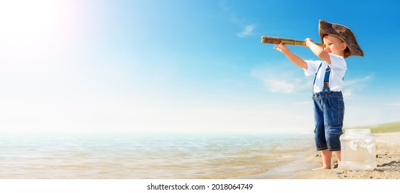 Kid Play On The Beach On A Hot Sunny Day. Little Girl Dressed As A Pirate Stands Barefoot On The Sandy Seashore With A Telescope. Child With A Toy Fish Dreams Of Travel And Adventure.