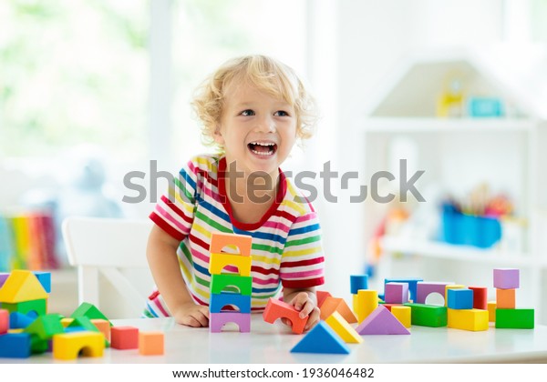 Kid playing with colorful toy blocks. Little boy\
building tower of block toys. Educational and creative toys and\
games for young children. Baby in white bedroom with rainbow\
bricks. Child at home.