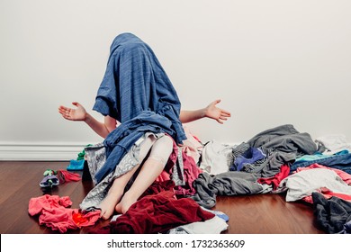 Kid playing with face covered. Cute Caucasian girl sorting clothes. Adorable funny child arranging organazing clothing. Kid with messy stack of clothes things on floor. Home chores housework.
