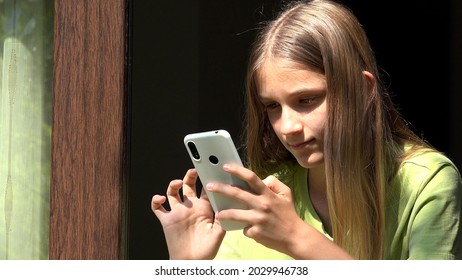 Kid Playing On Smartphone At Window, Child Browsing Internet, Young Girl Using Smart Phone 