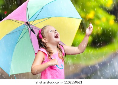 Kid playing out in the rain. Child with umbrella play outdoors in heavy rain. Little girl caught in spring shower. 