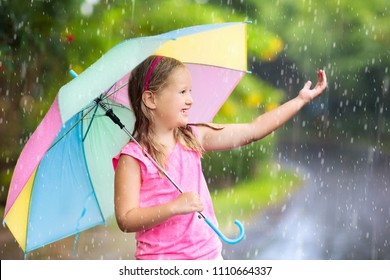 Kid playing out in the rain. Children with umbrella play outdoors in heavy rain. Little girl caught in first spring shower. Kids outdoor fun by rainy autumn weather. Child running in tropical storm.