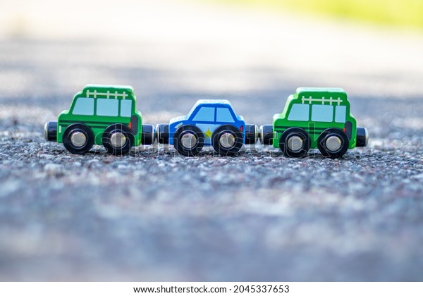 A kid is playing\
with some wooden cars, united like a train,magnet connections,on\
the asphalt, outside. Concept: playing outdoor, summertime, eco\
toys. police car, bus