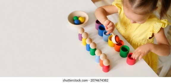 Kid Plays With An Educational Toy That Helps To Learn Colors At The Kindergarten Table. A Banner With Copy Space. Preschool Children's Development School. Fine Motor Skills Of Hands.