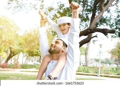 Kid Plays Flying Super Man. Side View Of Smiling Young Arabic Boy. Arab Father And Son Concept For Family In The Middle East. Man And Kid On Kandora Dish Dash