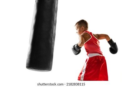 Kid Practicing Punch On Punching Bag. Beginner Boxer, Sportive Boy Wearing Boxing Gloves And Red Sports Uniform Training Isolated Over White Background. Sport, Achievemens, Challenges