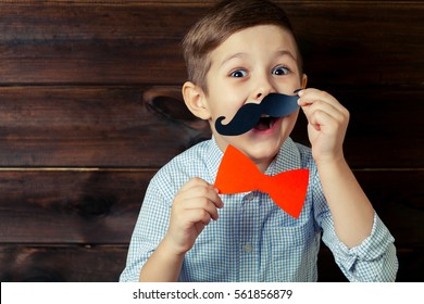 A Kid With Props For A Photo Booth. Surprised Child With The Requisite Mustache On Wooden Background. Event, Holiday, Party.