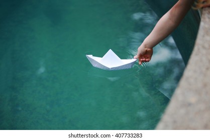 A Kid Putting A Paper Boat Into Water