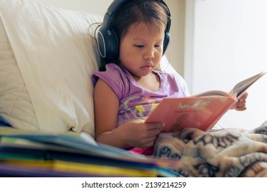 A kid reading in her room with books and listening on her headphones. Children literature and learning how to read.