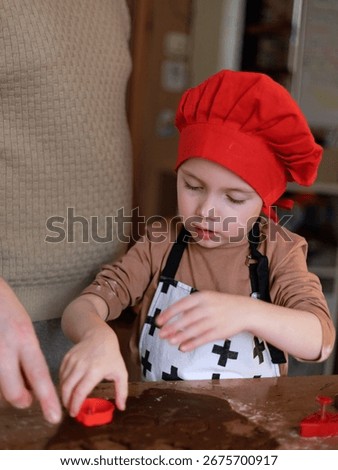 Kid with red chef hat making gingerbread with parent, joyful Christmas tradition of baking together. Copy space.