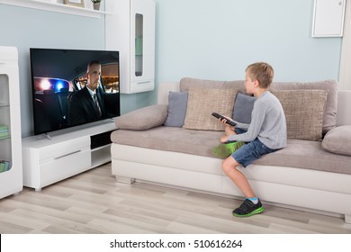 Kid With Remote Control Sitting On Couch Watching Movie On Tv