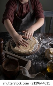 Kid Rolling Dough On Wooden Table With Ingredients Flour, Oil, Salt, Dark Background. Copy Space. Home Bakery Concept, Kitchen Cooking Story.