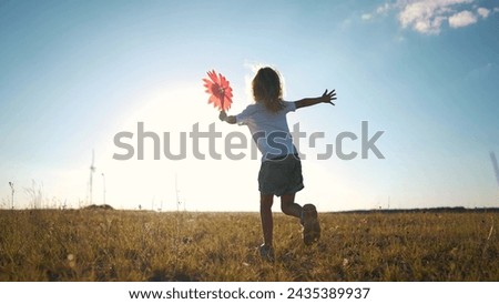 kid run pinwheel. little baby girl silhouette play with windmill toy wind in the park. happy family kid dream concept. baby girl play toy pinwheel glare of the sun at sunset in the fun park
