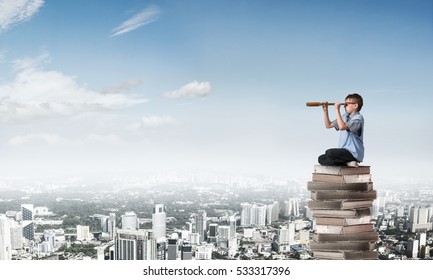 Kid of school age sitting on pile of books and looking in spyglass - Shutterstock ID 533317396