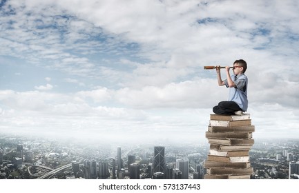 Kid of school age sitting on pile of books and looking in spyglass - Shutterstock ID 573137443