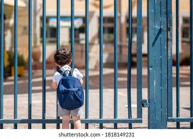 Kid with school backpack look on schoolyard towards an open entrance or exit door. Schools and preschools remain locked for children during lockdown, coronavirus pandemic and second wave of covid-19. - Shutterstock ID 1818149231