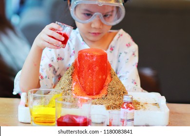 Kid Science Experiment Of Volcano Or Baking Soda And Vinegar Volcano Eruption For Kid.Girl With Eyeglasses Pouring Vinegar That Added Food Coloring Into The  Container Of Baking Soda And Observing. 