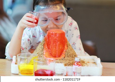 Kid Science Experiment Of Volcano Or Baking Soda And Vinegar Volcano Eruption For Kid.Girl With Eyeglasses Pouring Vinegar That Added Food Coloring Into The  Container Of Baking Soda And Observing. 