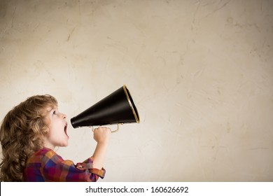 Kid shouting through vintage megaphone. Communication concept.