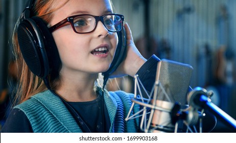 Kid singing in studio.Little girl singing a song.Front view close up. Kid wearing headphones attending singing class.