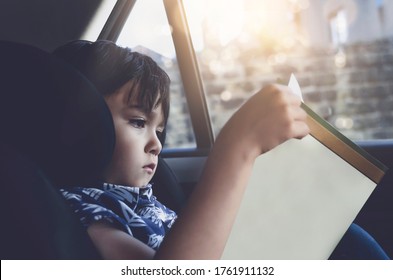 Kid Siting On Car Seat And Reading A Book, Little Boy Sitting In The Car In Child Safety Seat, Portrait Of Toddler Entertaining Himserf On A Road Trip. Concept Of Safety Taveling By Car With Children