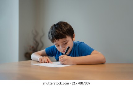 Kid siting on table doing homework,Child boy holding black pen writing on white paper,Young boy practicing English words at home. Elementary school and home schooling, Distance Education concept  - Powered by Shutterstock