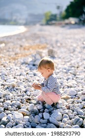 Kid Sits On A Pebble Beach And Holds A Pebble In His Hand. Side View