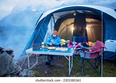 Kid, Sitting Around Campfire At Night, Enjoying Wild Camping, Family Vacation In Norway