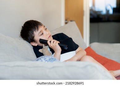 Kid Sitting On Sofa Watching TV, A Boy Holding Remote Control And Looking With Deep In Thought, Positive Child Lying On Sofa Enjoy Watching Cartoon On TV, Kid Relaxing At Home On Weekend