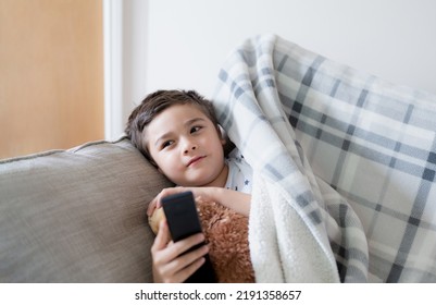 Kid Sitting On Sofa Watching TV, A Boy Holding Remote Control And Looking Up With Smiling Face, Positive Child Lying On Sofa Enjoy Watching Cartoon On TV, Kid Relaxing At Home On Weekend