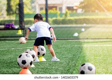 Kid Soccer Player Is Start Training To Shoot Ball On Marker Cone To Goal On Artificial Turf. Asian Boy Soccer Player In Football Academy.