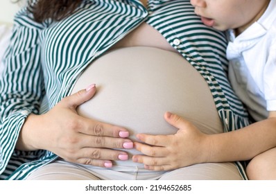 Kid Speaking Telling Stories To Baby Brother In Mommy Mother Belly Uterus.cute Adorable Child Holding Ear Bonded On Tummy Pressing With Hand Speaking Smiling.bedroom Interior,bright Beige Colors.hug