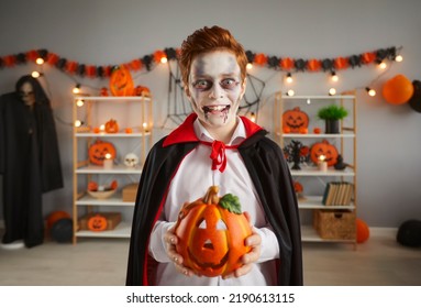 Kid In Spooky Halloween Vampire Costume. Child Dressed Up As Count Dracula Holding Jack-o-lantern Decor. Portrait Of Boy In Black Cape With Eyes, Excited Expression And Fake Blood Makeup On