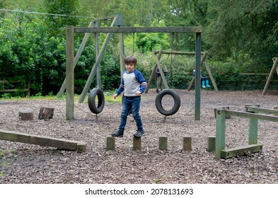 Kid Standing On Wooden Climbing In Playground, Child Enjoying Activity In A Climbing Adventure Park,  Selective Focus Of Child Playing On Balance Beam Outdoor Playground.