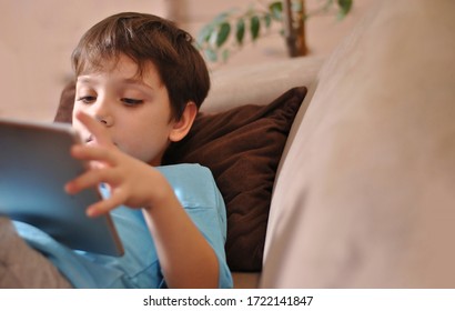 Kid stays home for reading and preparing home task. Stay at home for safety. Reading online. Little boy laying on the sofa resting and watching at the tablet. Children with digital gadget.