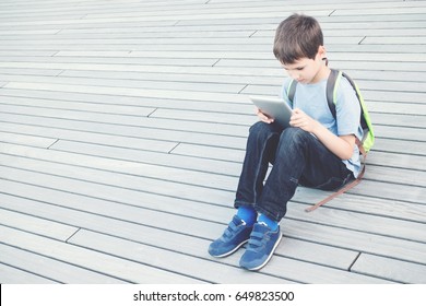 Kid With Tablet Computer Sitting On Wooden Terrace Outdoors