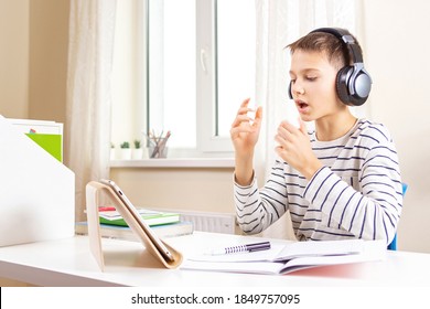 Kid with tablet computer sitting at table with books and having video call, virtual online leasson at home - Powered by Shutterstock