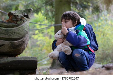 Kid With Teddy Bear Sitting Under The Big Tree Pointing Finger Up And Looking, Curious Boy Looking At Some Things On Wooden Statue. Child Having Fun Adventure In Autumn Forest